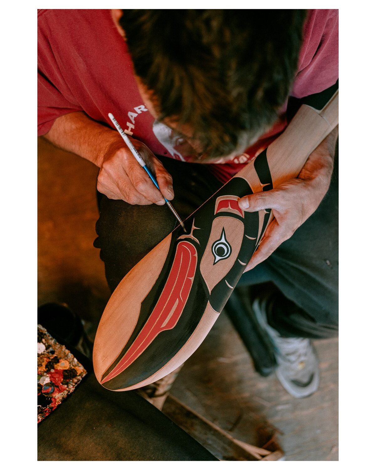 Ross Henderson laying red and black paint into a carved formline